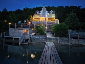 A waterfront property with a dock leading to a house with multiple levels and a stone chimney. - Tranquil Cove | Lakefront Cabin w. Wraparound Deck + Entertainment Room (Douglas Lake)