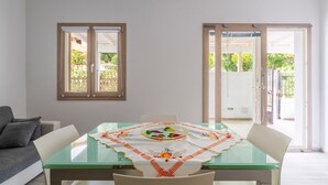A dining area with a glass table, white chairs, and a tablecloth with a fruit pattern. - La Casa di Samu - White Apartment (Arbatax)