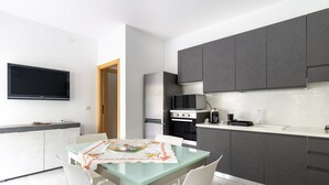 A modern kitchen with dark cabinets, a flat-screen TV, a dining table with chairs, and a microwave. - La Casa di Samu - White Apartment (Arbatax)