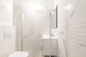 Un baño moderno con cabina de ducha de vidrio, un lavabo blanco y un revestimiento de mármol en la pared.