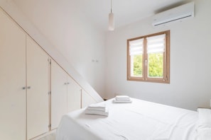Een slaapkamer met een bed, een raam met zonwering, een airconditioning en een kledingkast.