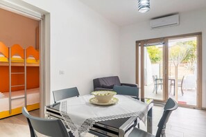 Een kamer met een eettafel, stoelen, een stapelbed en een schuifdeur die leidt naar een buitenruimte.