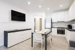 A modern kitchen with white cabinets, a black countertop, a built-in stove, and a flat-screen TV mounted on the wall.
