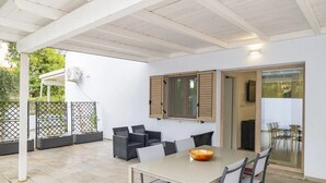 Une terrasse couverte avec une table et des chaises, une fenêtre avec des volets et une vue sur l’extérieur.