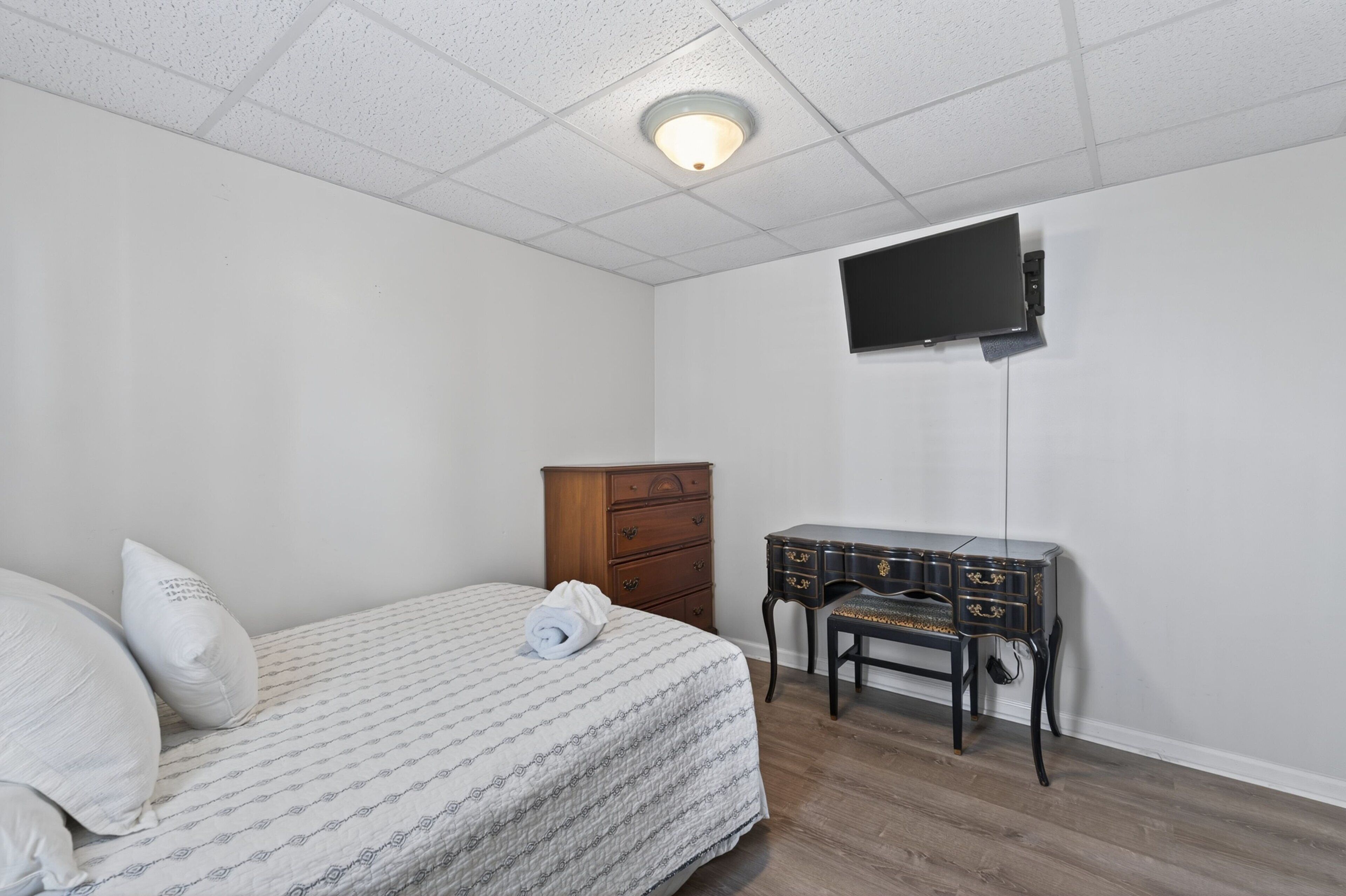 A bedroom with a bed, a dresser, a desk, and a television mounted on the wall.