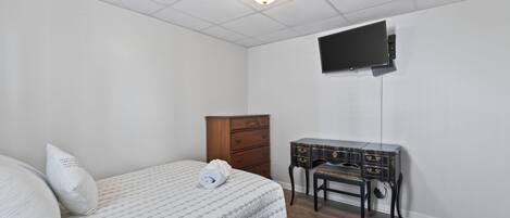 A bedroom with a bed, a dresser, a desk, and a television mounted on the wall.