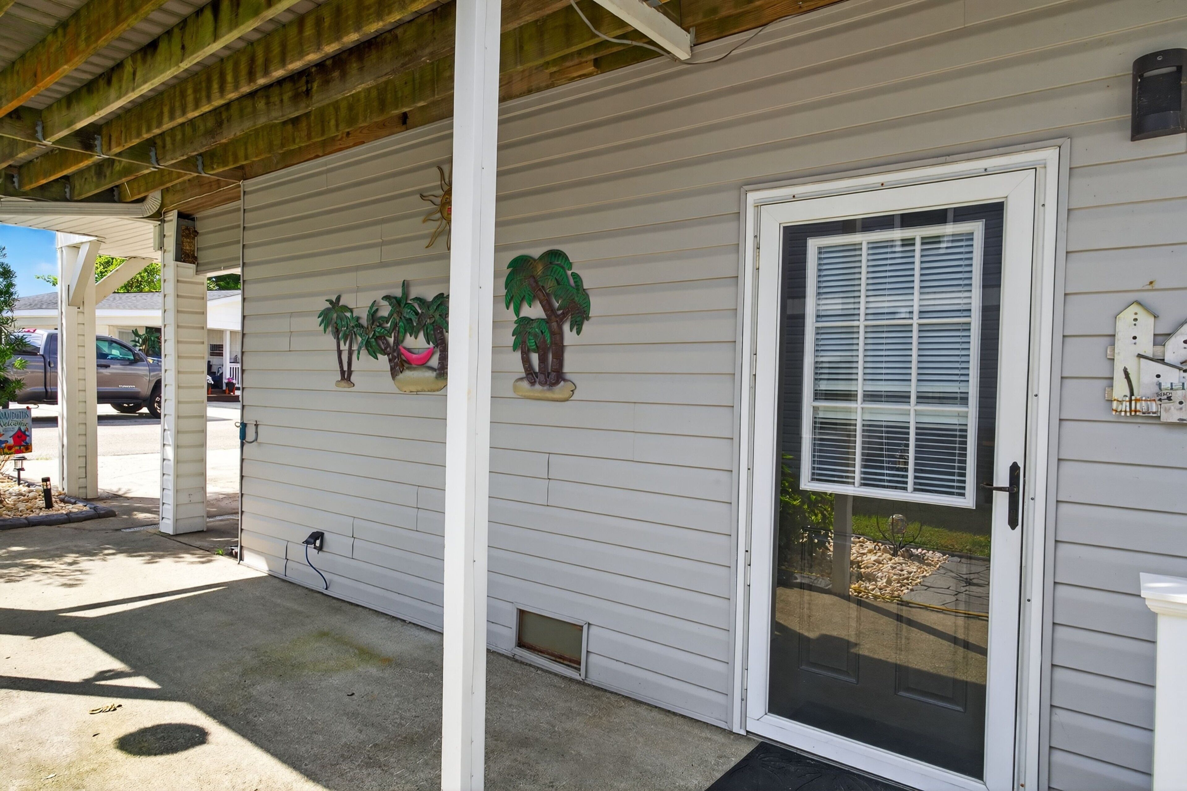 A house with a covered porch, a sliding glass door, and decorative palm trees.