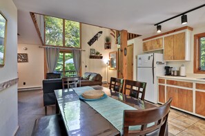 A dining area with a wooden table and chairs, a kitchen with wooden cabinets, and a large window with curtains.