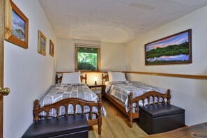 A bedroom with two wooden beds, a window, a painting, and a wooden nightstand.