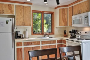 A kitchen with wooden cabinets, a window, a refrigerator, a microwave, a kettle, and a coffee maker.