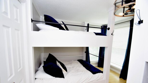 A bunk bed room with a white headboard, a window with blinds, and a door. - Aronimink 1b 2 Bedroom Condo (Ocean City)