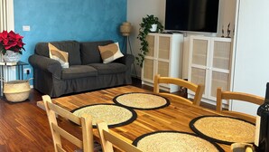 Un salon moderne avec un mur d’accent bleu, un canapé gris et une table à manger en bois agrémentée de sets de table en fibres tressées.