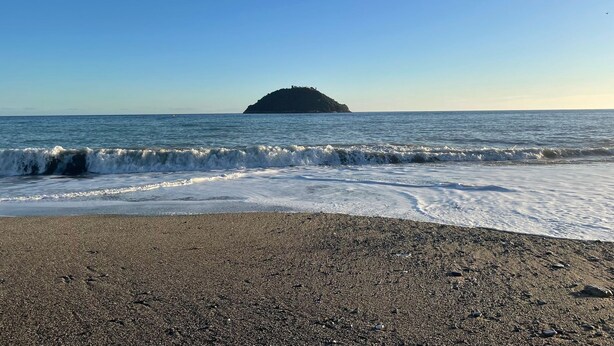 Une plage au rivage rocheux, avec une petite île qui se profile à l’horizon.