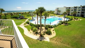 Un espace piscine avec vue sur la plage, entouré de palmiers et bordé d’un immeuble doté de balcons.