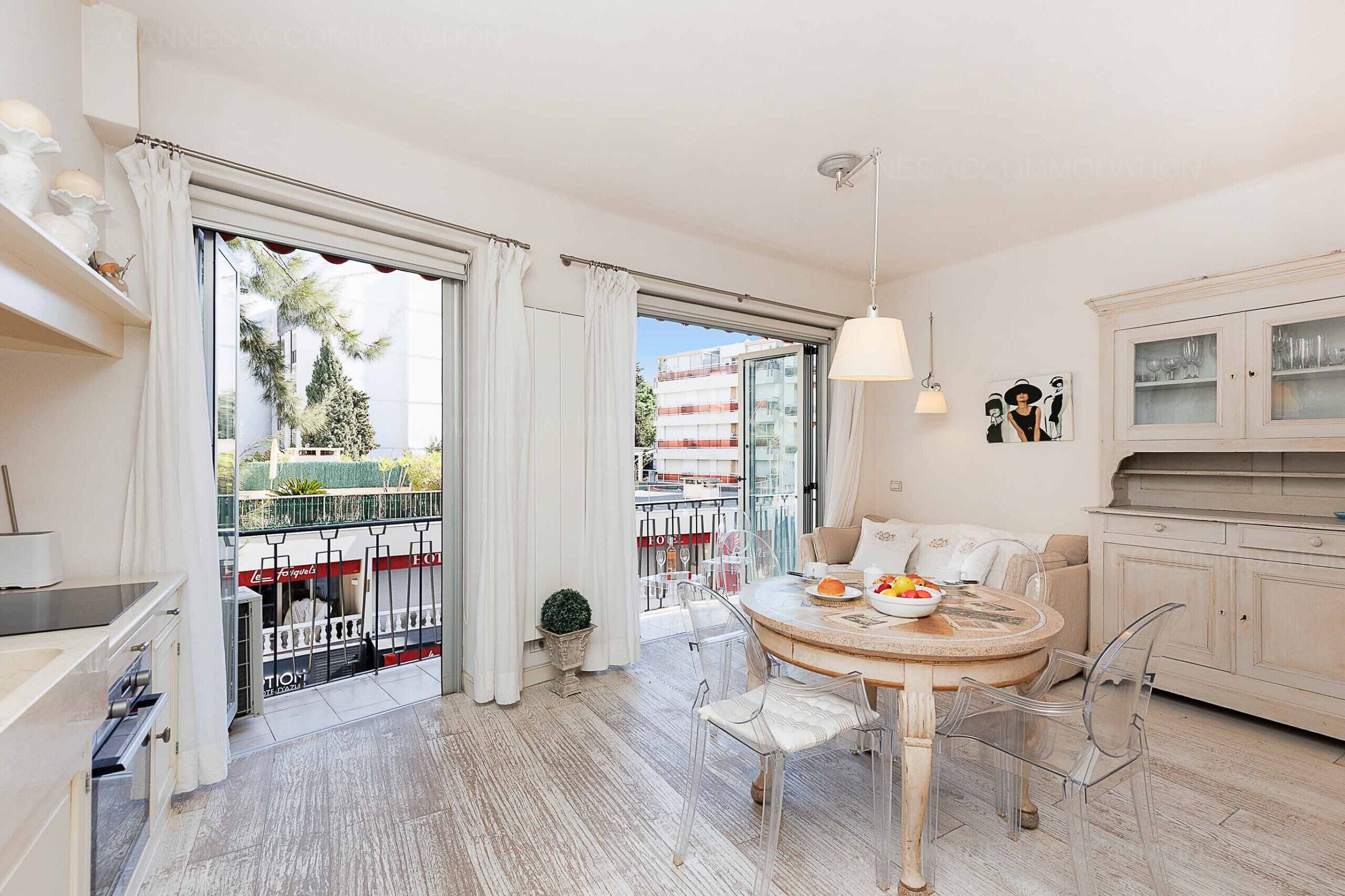 A modern living room with a round dining table, clear chairs, a sofa, and a kitchen area with cabinets.