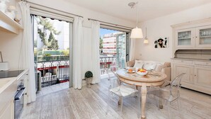 A modern living room with a round dining table, clear chairs, a sofa, and a kitchen area with cabinets. - CG Armenonville White-2811-very charming studio near the Croisette (Cannes)
