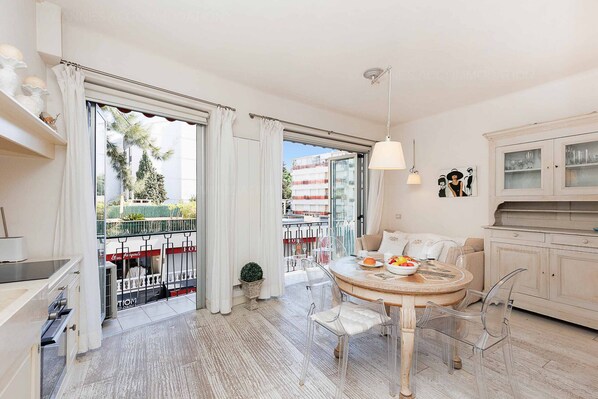 A modern living room with a round dining table, clear chairs, a sofa, and a kitchen area with cabinets.