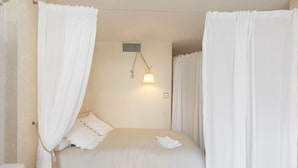 A neatly made bed with white bedding, a hanging lamp, and sheer curtains. - CG Armenonville White-2811-very charming studio near the Croisette (Cannes)