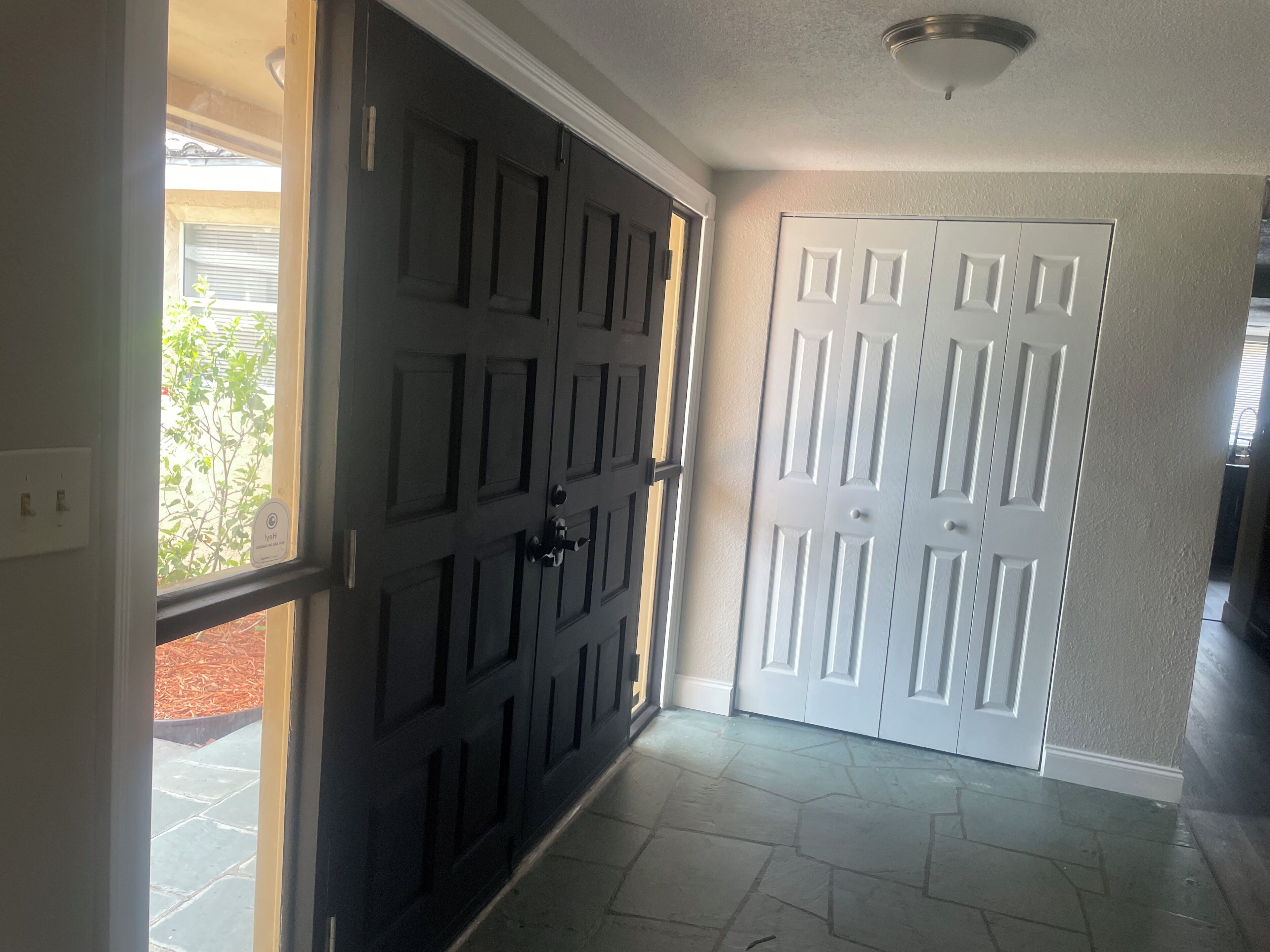 A hallway with two doors, one black and one white, leading to a room with a stone floor.