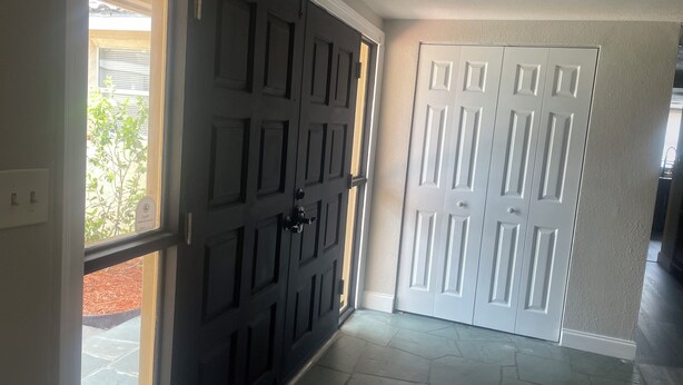 Un pasillo con dos puertas, una negra y otra blanca, que conducen a una habitación con suelo de piedra.