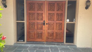 Puerta doble de madera con tallas intrincadas, un acceso empedrado de piedra y dos faroles fijados a la pared.