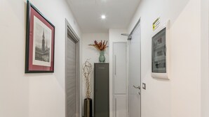 Un couloir avec un tableau encadré, un vase contenant des branches séchées, une armoire et une porte.