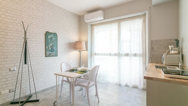 Une pièce moderne comprenant une table à manger, des chaises, un lampadaire et un coin cuisine équipé d’un four à micro-ondes.