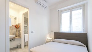 Une chambre à coucher avec un lit, une fenêtre et une salle de bain visible à travers une porte ouverte.