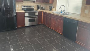 A kitchen with dark tiled flooring, stainless steel appliances, wooden cabinets, and a window with blinds. - Terrific 3-bedroom house with bird caged swimming pool in Spring Hill (Spring Hill)