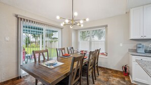 A dining area with a wooden table, chairs, a chandelier, and a view of the outdoors through large windows. - Space & Sunshine Retreat/3BR Near NASA & NRG (Houston)