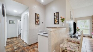 A spacious kitchen with a granite countertop and a sink, a dining area with a floral chair, and a hallway leading to another room. - Space & Sunshine Retreat/3BR Near NASA & NRG (Houston)