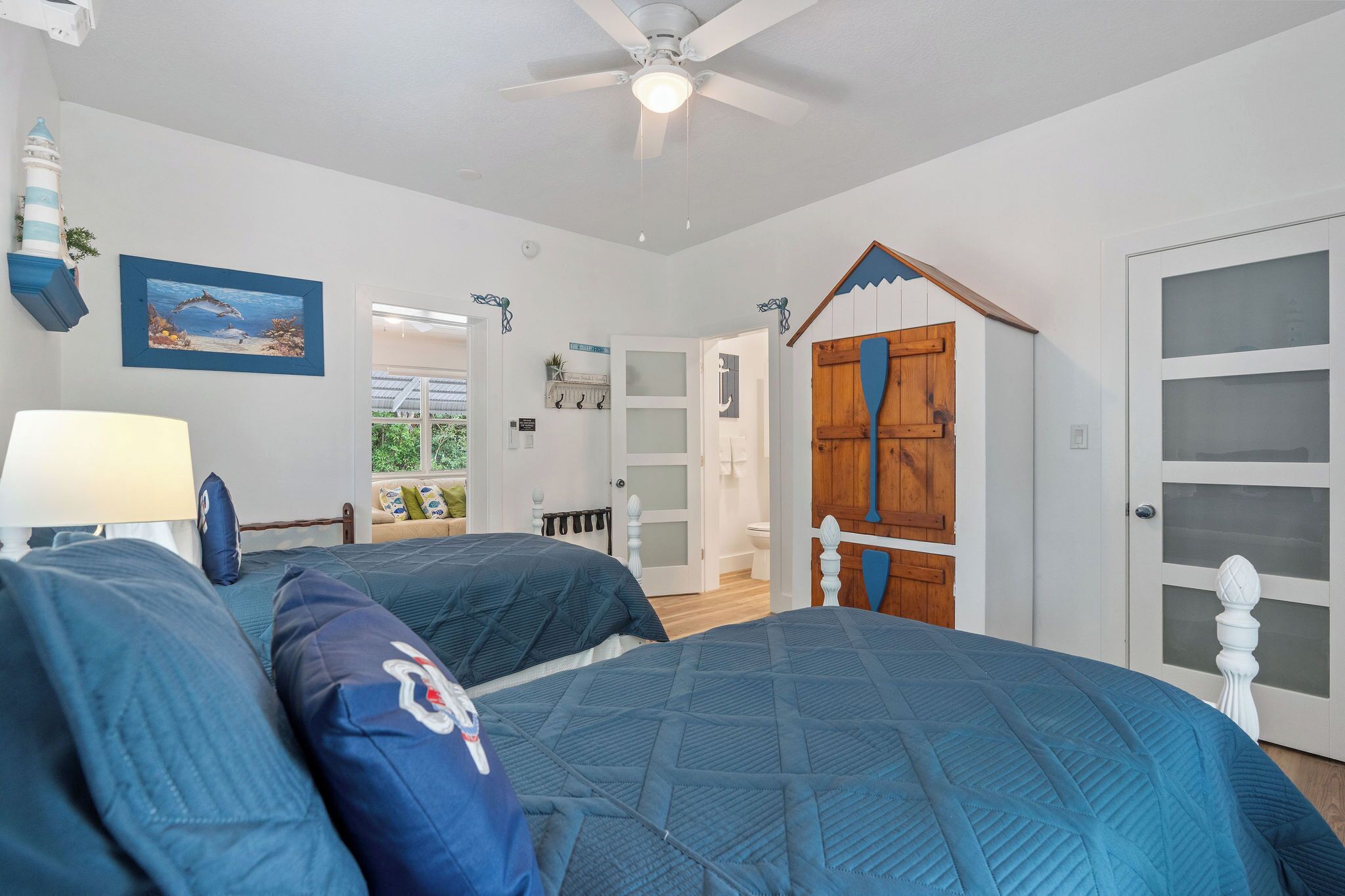 A bedroom with two beds, a ceiling fan, a nightstand, a lamp, and a door with frosted glass panels.