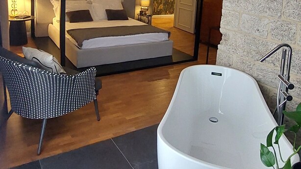 Un dormitorio moderno con una cama con dosel, una bañera grande y una zona de estar.