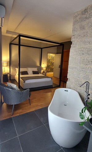 A modern bedroom with a four-poster bed, a large bathtub, and a seating area. - Historic House IN THE TOWER B&B (Ascoli Piceno)