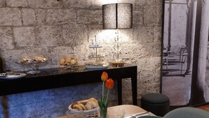 Un comedor con pared de ladrillo, una mesa dispuesta con platos, vasos y diversos alimentos, incluyendo pasteles y carnes.