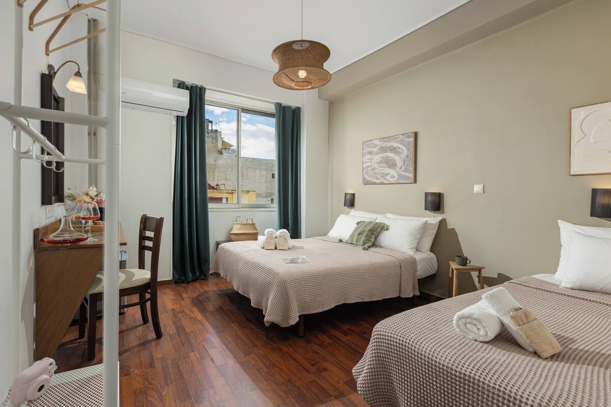 A hotel room with two beds, a dining area, and a view of the city.