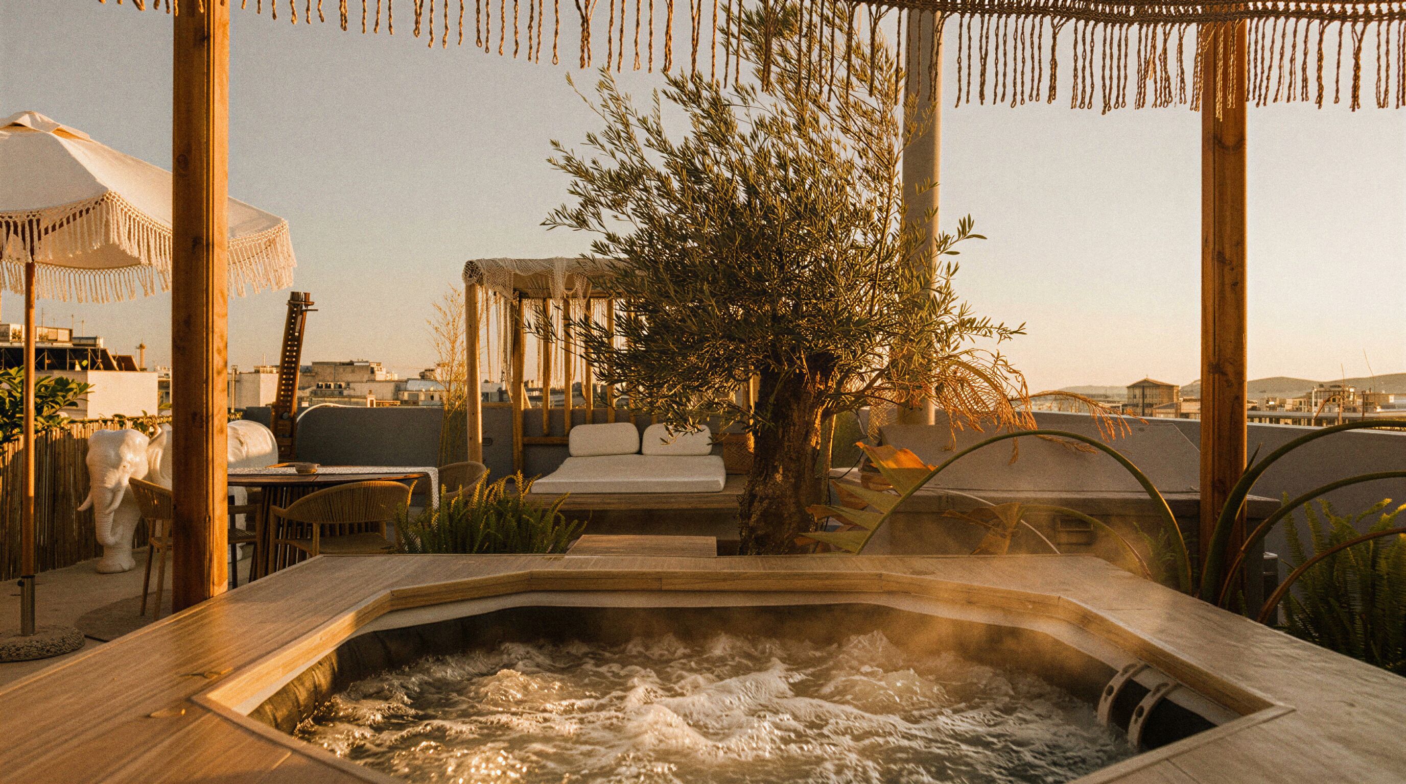 A hot tub with a wooden edge, surrounded by outdoor furniture and a tree.
