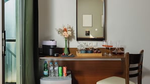 Ein Hotelzimmer mit Schreibtisch aus Holz, Blumen in einer Vase, einem Spiegel und einer Minibar.