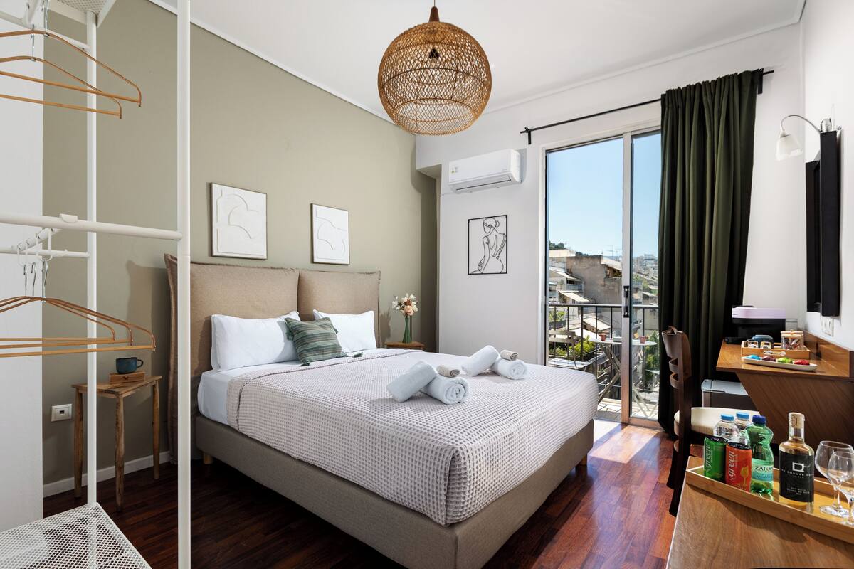 A hotel room with a bed, a desk with a computer, a balcony with a view, and a hanging light fixture.