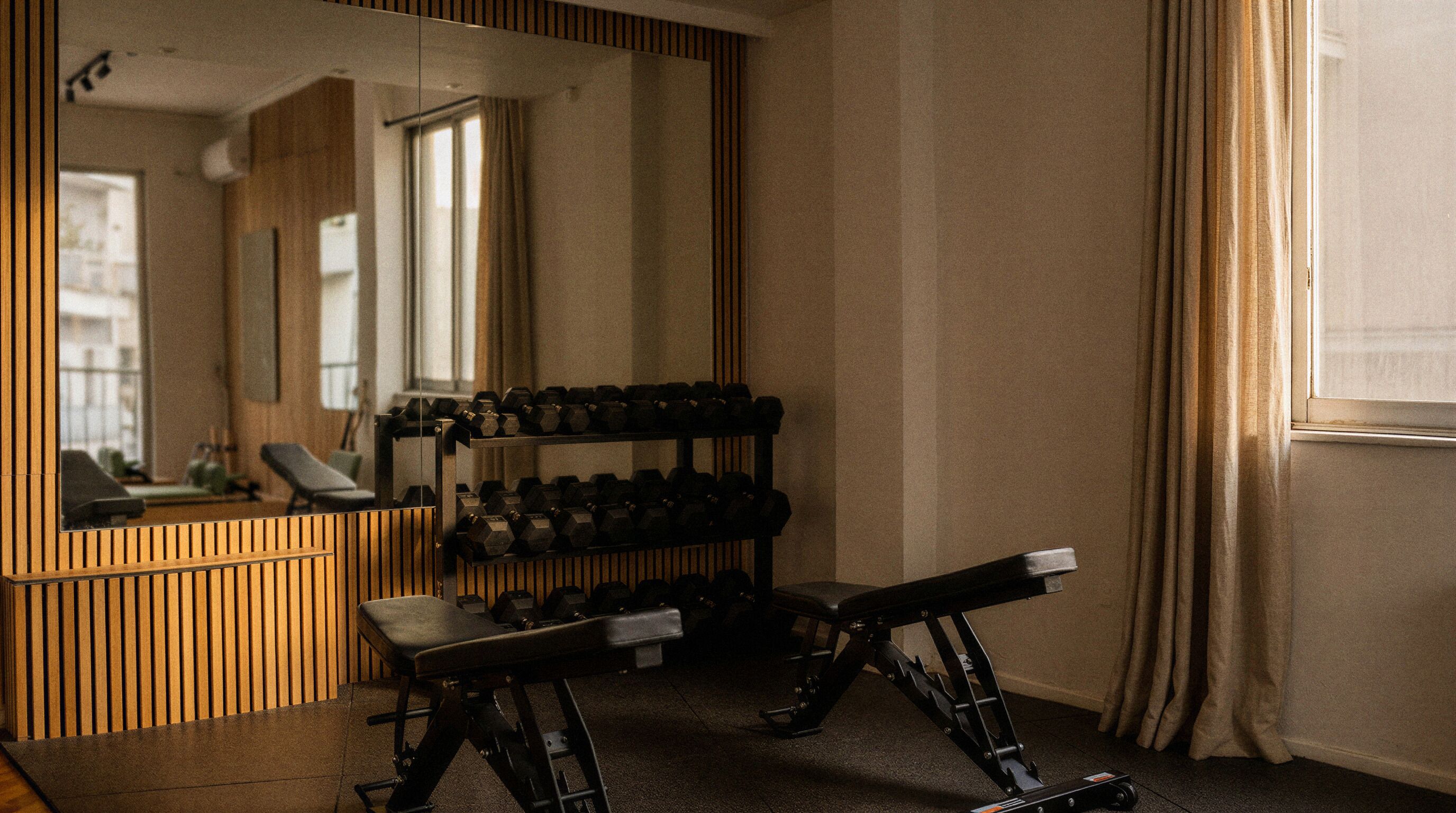 A gym with exercise equipment, a bench, and a mirror reflecting the room.