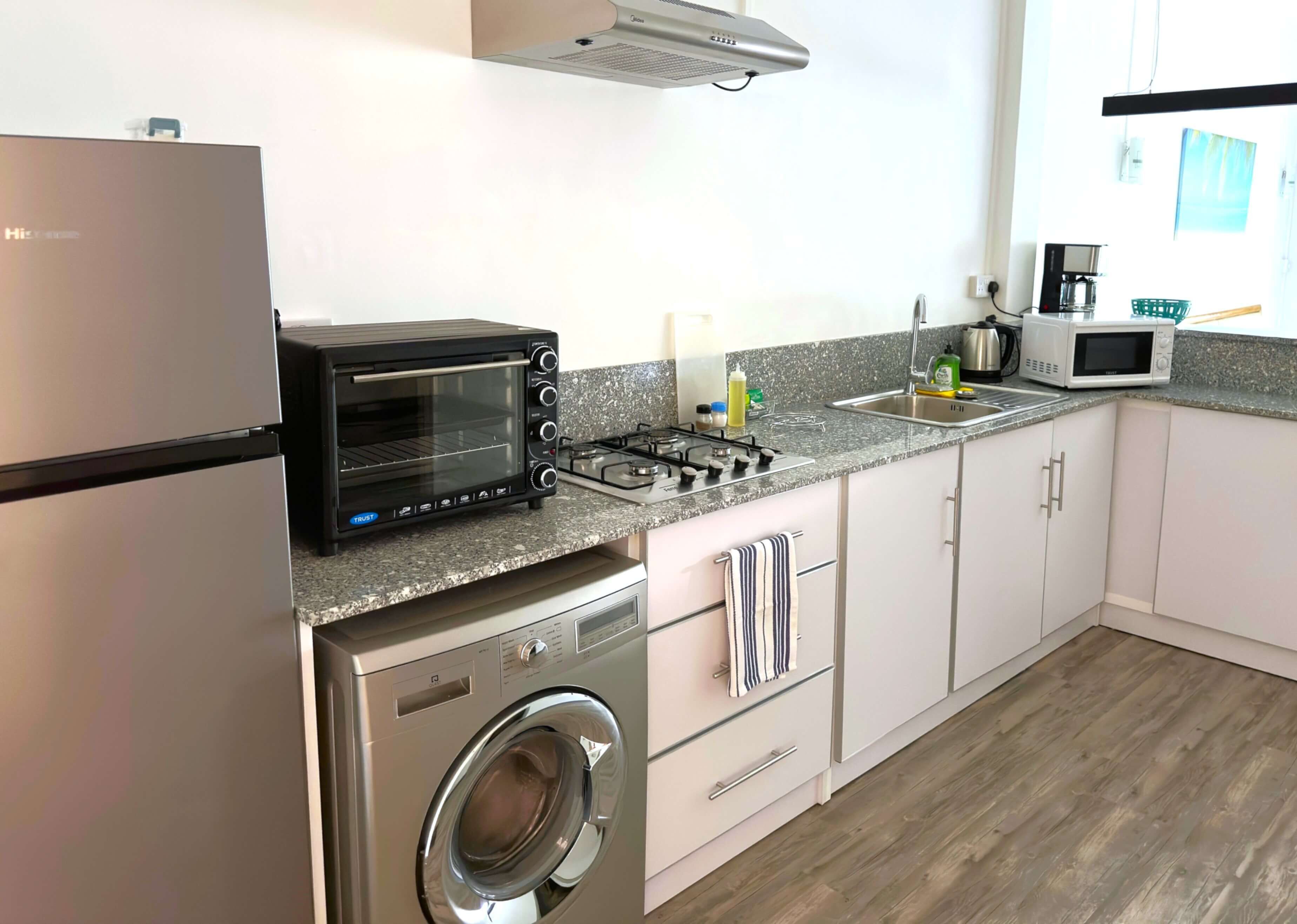 Une cuisine compacte équipée d’un lave-linge intégré, d’un four grille-pain, d’un four à micro-ondes et d’une cuisinière à gaz.