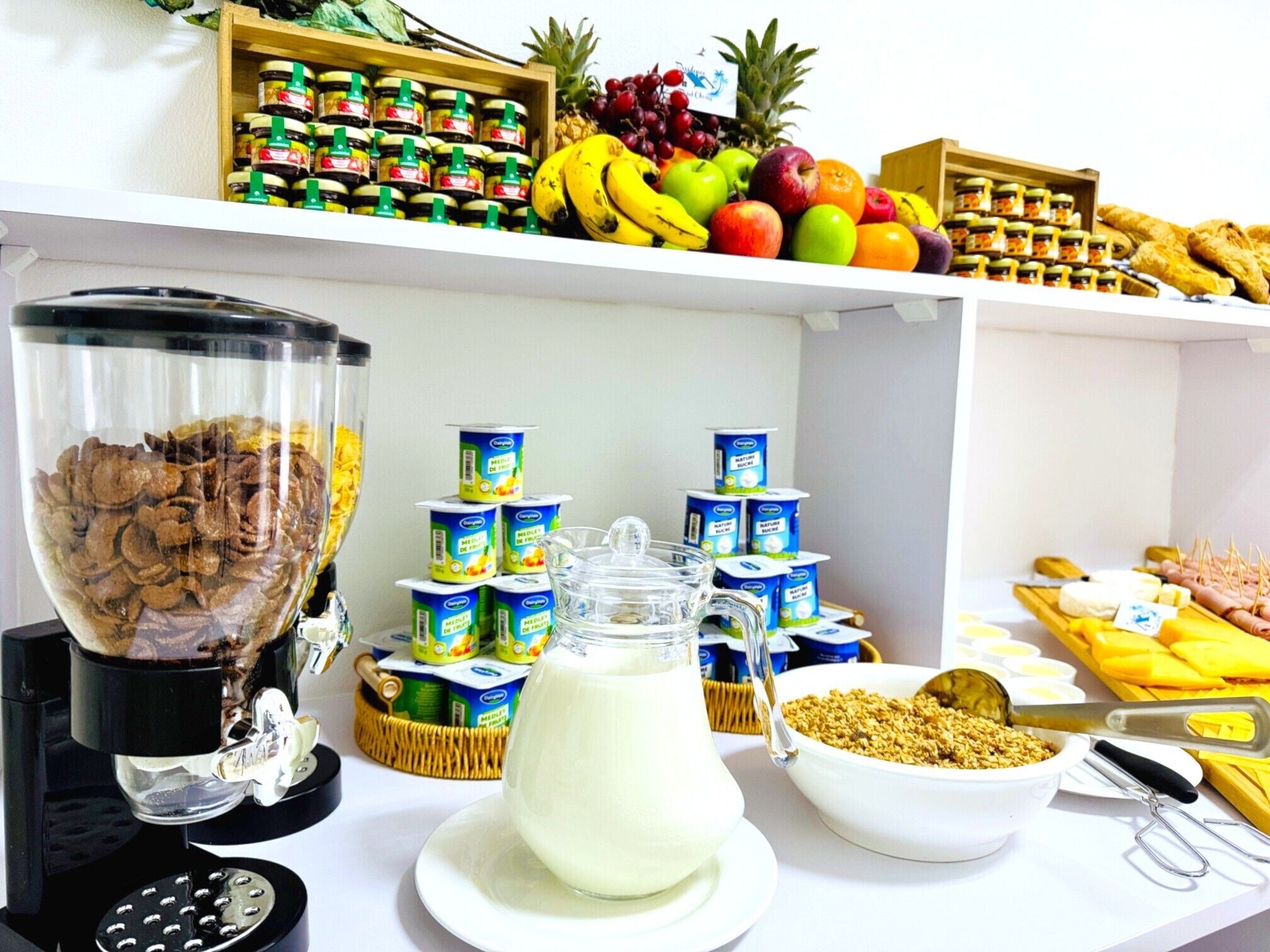En morgenmadsbuffet med cornflakes, mælk, yoghurt samt et udvalg af frugter og kager.
