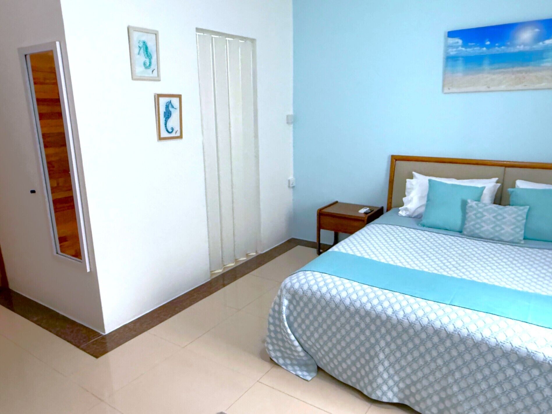 A hotel room with a bed, a nightstand, a door, and two framed pictures on the wall.