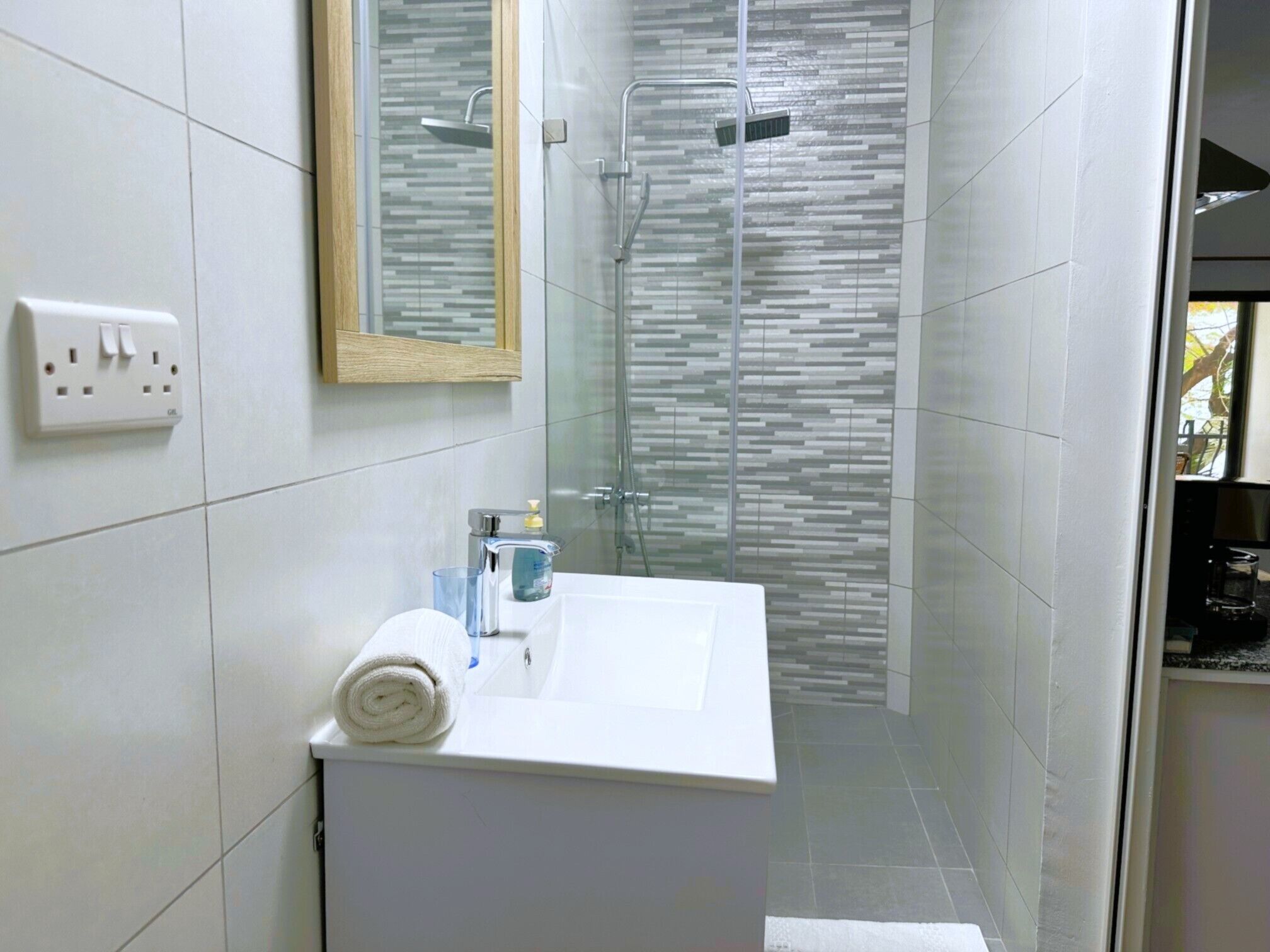 A modern bathroom with a glass shower enclosure, a white sink with a towel, and a mirror above it.