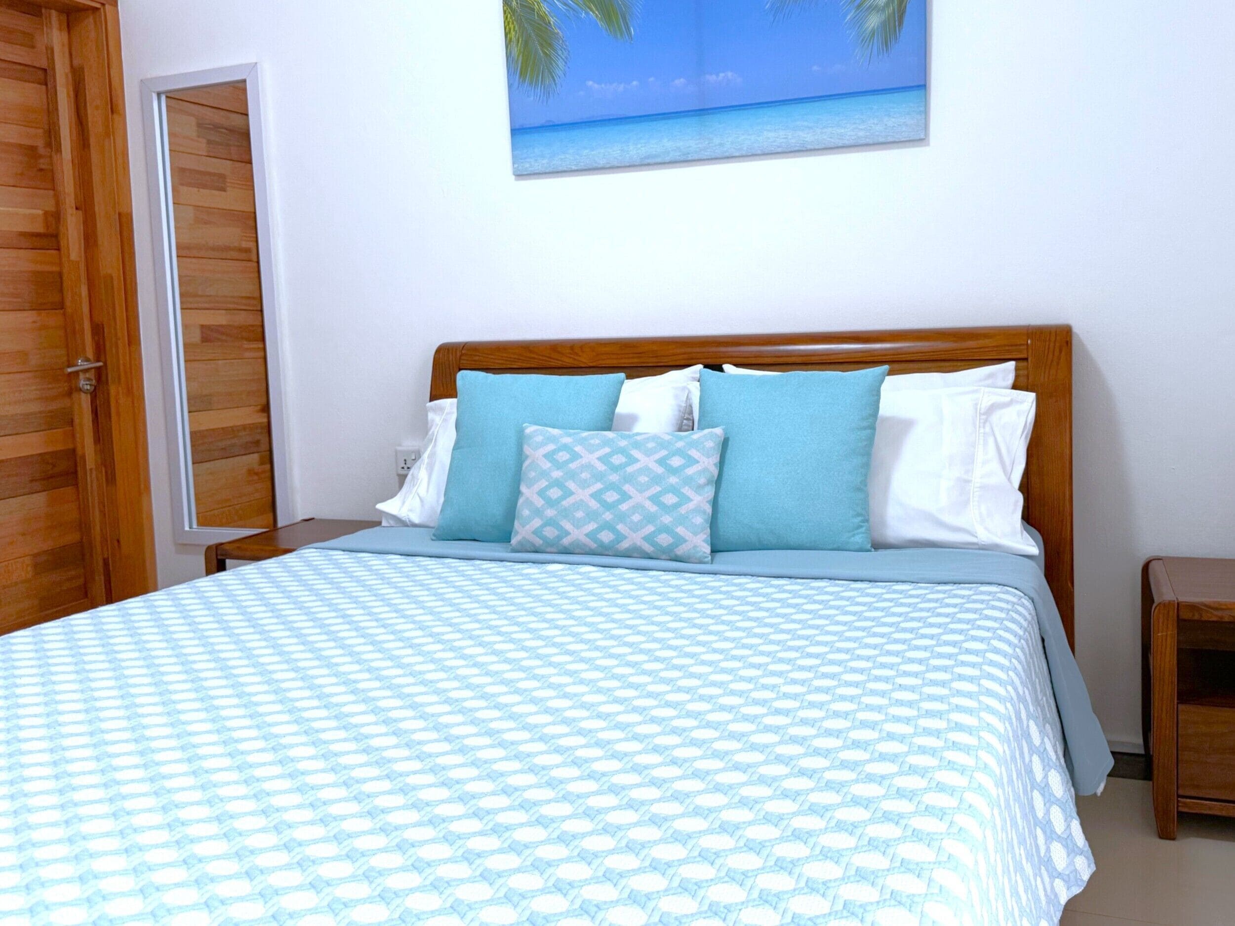 Un letto rifatto con una coperta a righe blu e bianche, una testiera in legno e un quadro appeso al muro raffigurante una spiaggia.