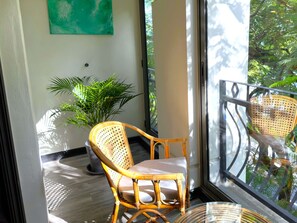 A balcony with a wicker chair, a potted plant, and a view of greenery. - Residence Le Point Choisy (Grand-Baie)
