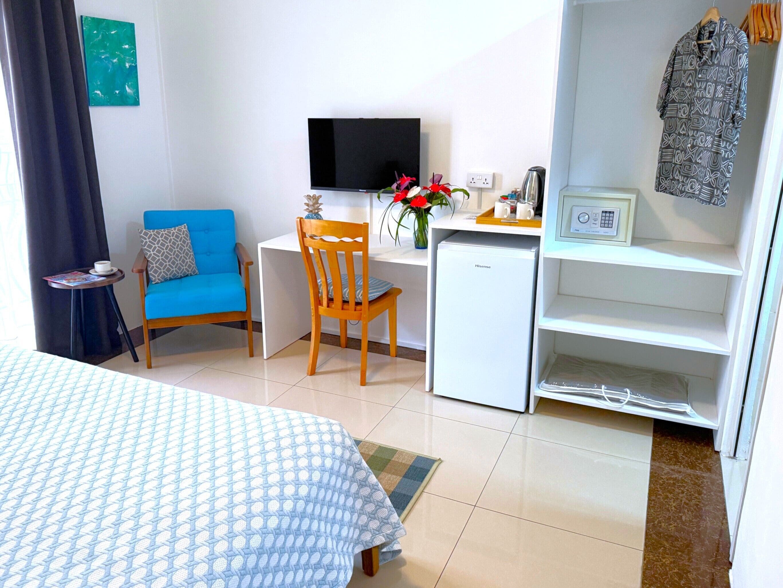 A hotel room with a bed, a desk, a chair, a small fridge, a TV, and a wardrobe.