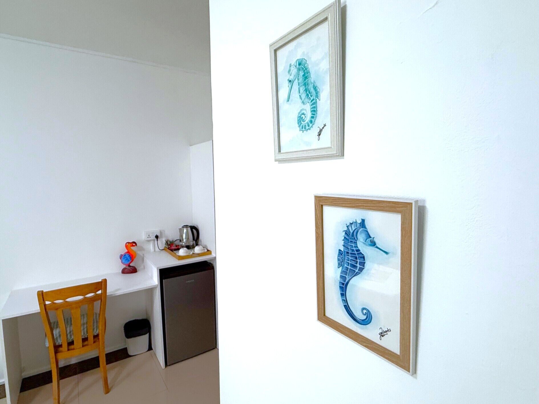 Una pequeña kitchenette con una silla de madera, un lavamanos y una cafetera. Hay dos obras de arte con la imagen de caballitos de mar en la pared.