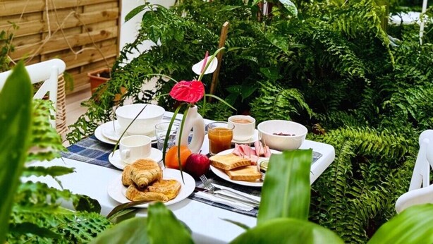 Un espace de restauration en plein air, avec une table dressée pour le petit-déjeuner, entouré d’une végétation luxuriante.