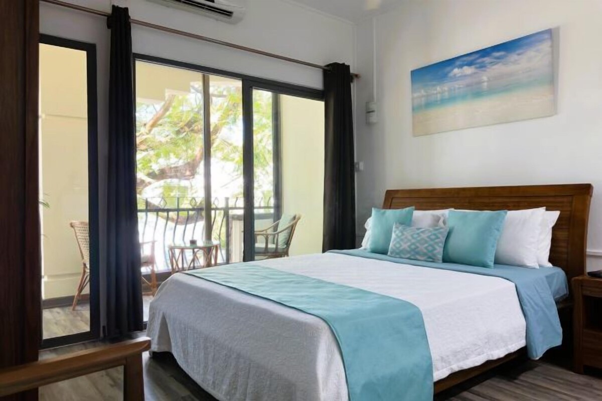Quarto com uma cama grande, vista para o exterior por uma porta deslizante e um quadro na parede.